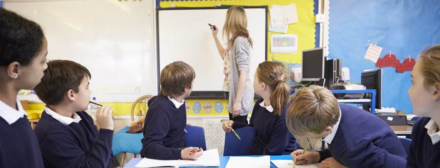 A classroom with a teacher writing on a whiteboard.